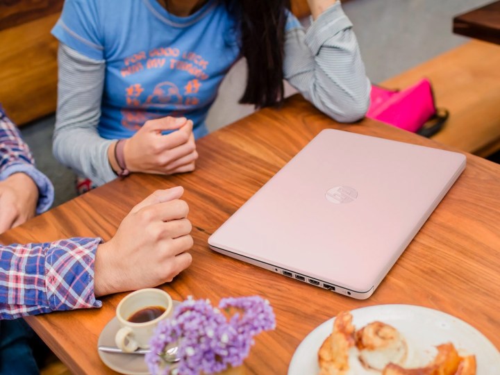 Một mẫu máy tính xách tay 14 inch HP Stream màu hồng đặt trên bàn cà phê trong khi mọi người trò chuyện.