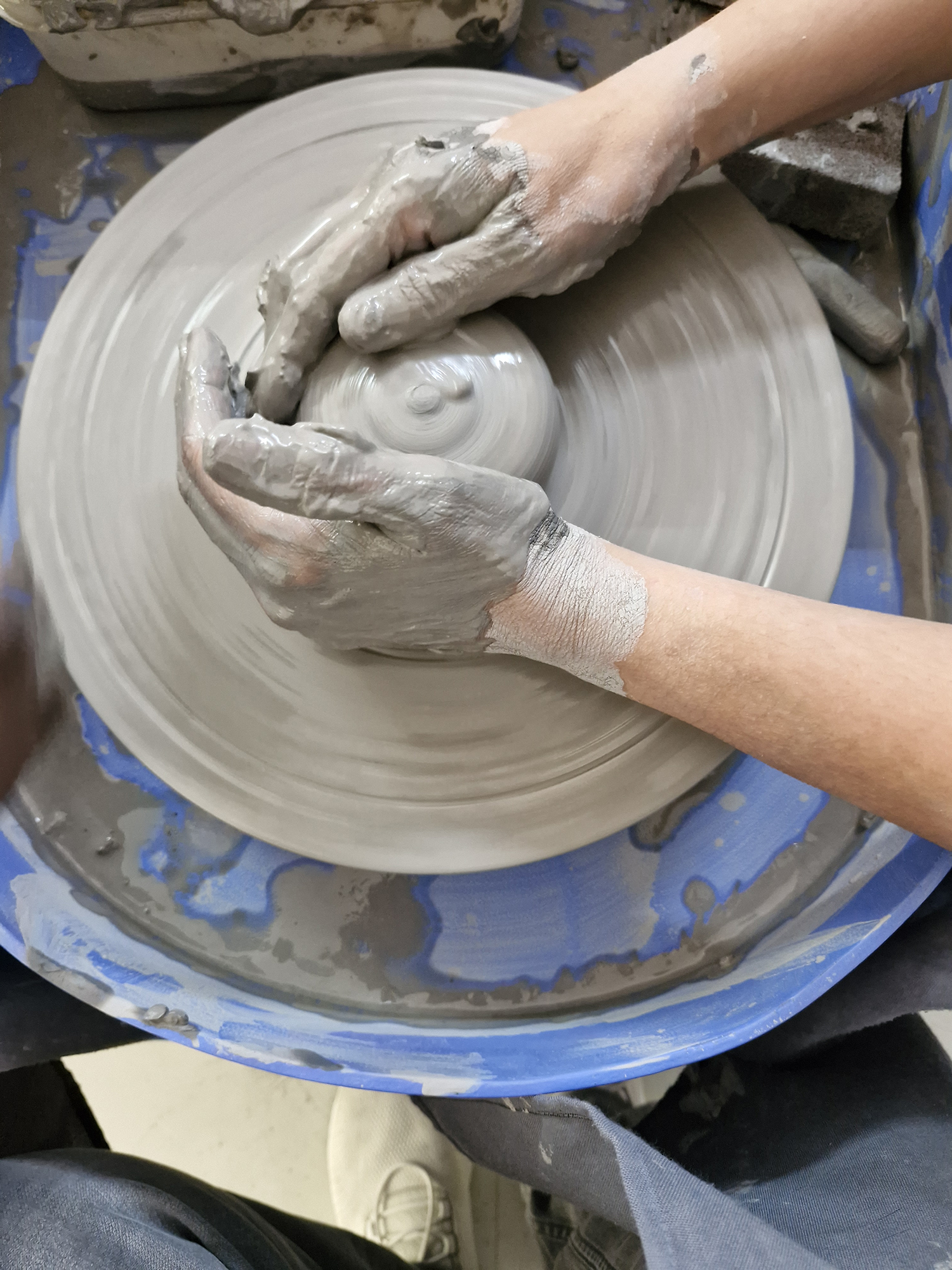 Hands on a potters' wheel photographed with the Samsung Galaxy S23 FE.