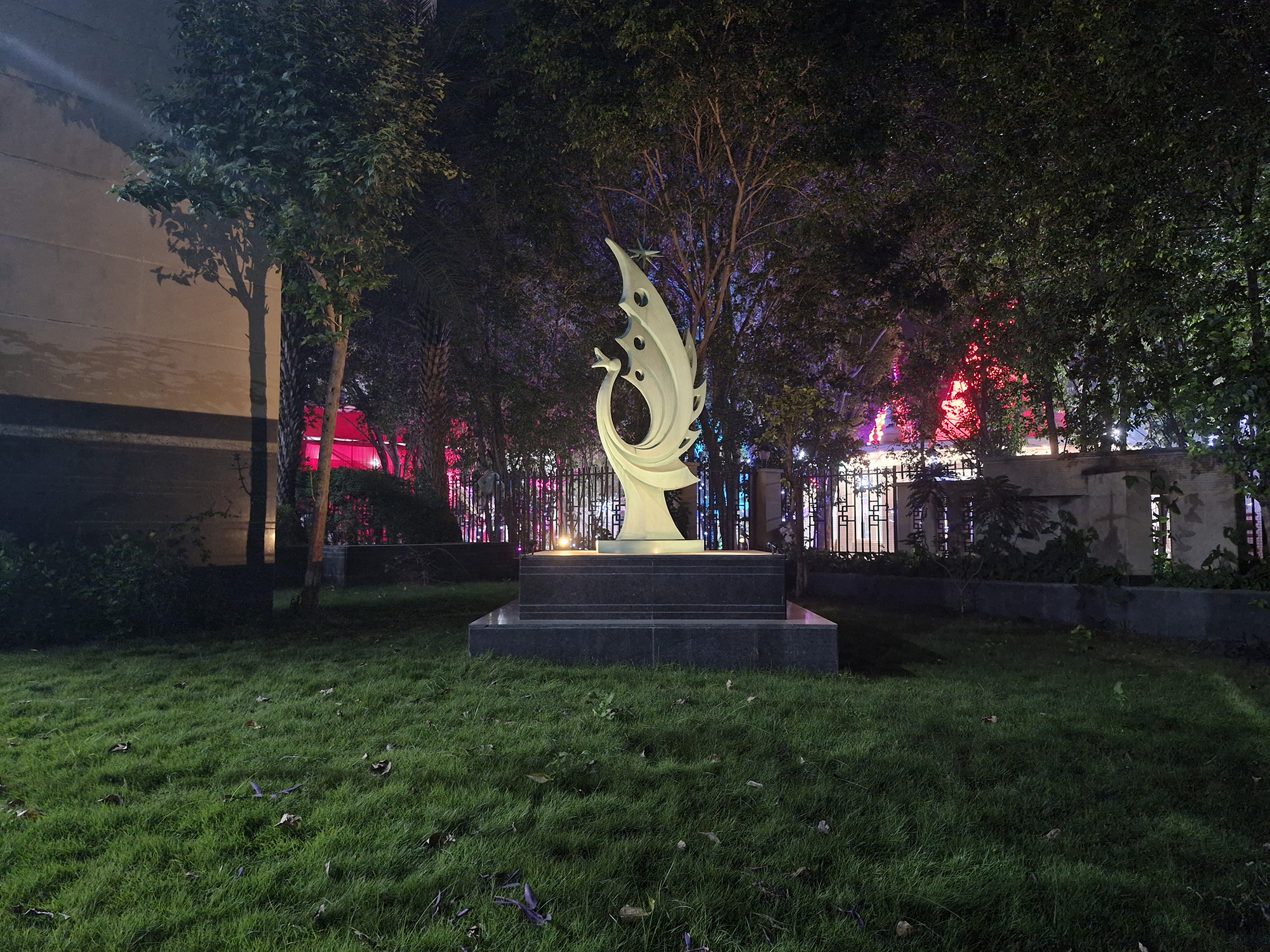 Green sculpture on a marble platform over grass photographed with the Samsung Galaxy S23 FE at night.