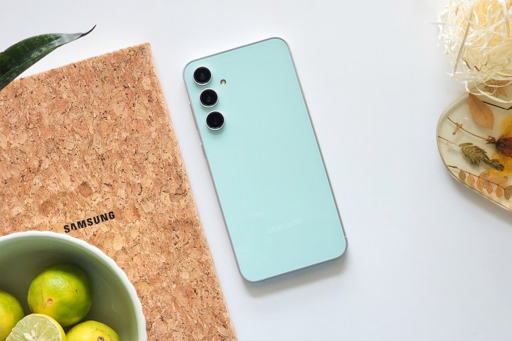 Samsung Galaxy S23 FE Mint Green color along with abowl of lemons, a Samsung notebook, and coaster.